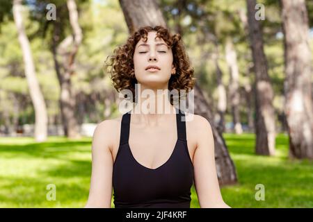 Nette Rotschopf Frau trägt sportliche Kleidung stehen im Stadtpark, im Freien tun Yoga einfache Sitzposition, sukhasana Haltung entspannen atmen einfache Sitzposition, Stockfoto
