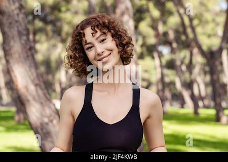 Junge Rotschopf-Frau in einem schwarzen Sport-BH, die auf dem Stadtpark steht und im Freien die Kamera anschaut, während sie posiert. Natürliches Schönheitskonzept. Schönes Mädchen. Pr Stockfoto