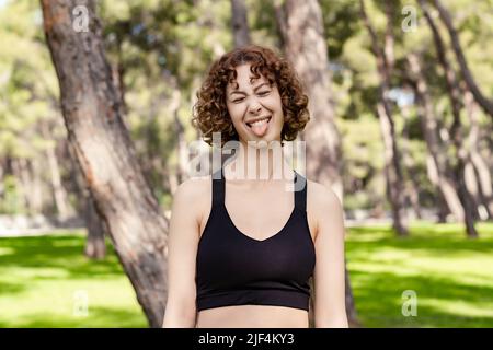 Nette Rotschopf Frau trägt sportliche Kleidung stehen auf Stadtpark, im Freien stehend Zunge aus glücklich mit lustigen Ausdruck. Emotionskonzept. Stockfoto