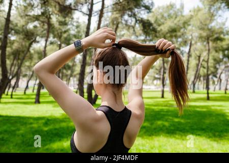 Junge Brünette Frau in sportlicher Kleidung im Stadtpark, im Freien binden ihre Haare in einem Pferdeschwanz, während Sie einige Training. Stockfoto