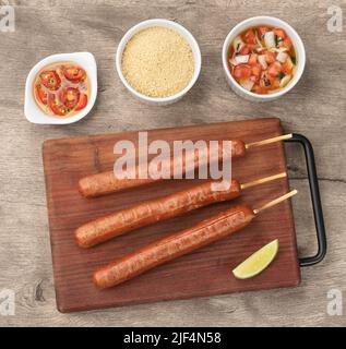 Schweinewurstspieße auf Holzbrett mit Farofa, Zitrone und Pfeffer. Stockfoto