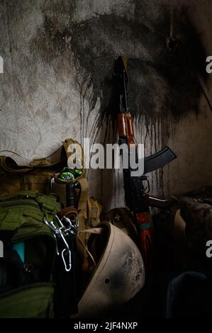 Das Maschinengewehr des ukrainischen Soldaten lehnt sich im Haus an die Mauer, der Krieg in der Ukraine, Waffen und Rüstungen in einem verlassenen Haus. Stockfoto