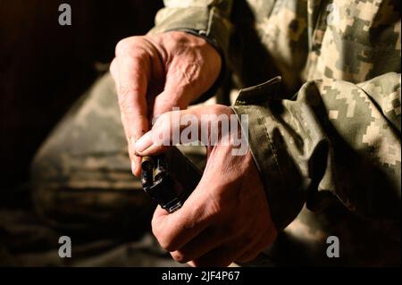 Das Magazin mit militärischen Kampfgewehren AK 74 füllen, einem Soldaten in einem Graben, der für ein Maschinengewehr Munitionsmaterial hält, der Krieg in der Ukraine. Stockfoto