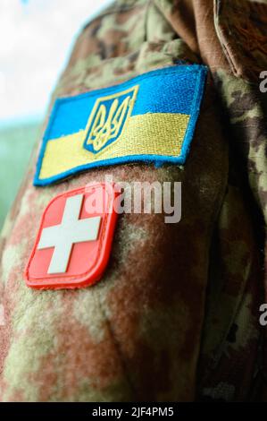 Militärisches Sanitäter-Zeichen. Chevrons auf der ukrainischen Militär-Pixel-Uniform, blau-gelbe Flagge und rotes Kreuz-Zeichen. Stockfoto