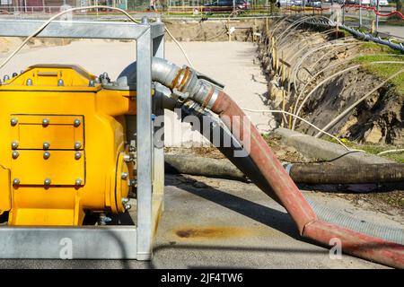 Große, tragbare, gelbe elektrische Wasserpumpe mit Schlauch zur Entwässerung der tiefen Grube des Gebäudefundaments Stockfoto