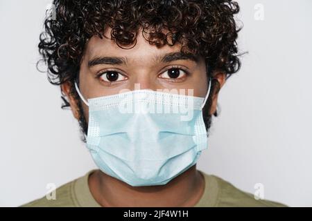 Junger Mann aus dem Nahen Osten, der in einer Schutzmaske über einer weißen Wand posiert Stockfoto