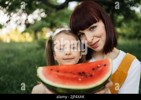 Picknick im Sommerpark. Nahaufnahme Porträt der alleinerziehenden Mutter mit kleinen Tochter ist in Essen Wassermelone Ruhe im Freien beschäftigt. Stockfoto