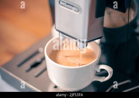 Moderne Kaffeemaschine mit einer teilweise vollen Tasse Kaffee auf dem Tisch in der Küche Stockfoto