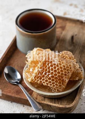 Honig in Waben in einer Untertasse mit Tee und Löffel auf Holztablett. Vertikale Ausrichtung Stockfoto