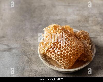Honig in Waben in einer Untertasse auf grünem texturierten Hintergrund, Textraum. Horisontale Ausrichtung Stockfoto