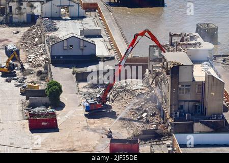 London, England - Juni 2022: Luftaufnahme eines mechanischen Baggers mit langem Arm, der ein altes Gebäude an der Themse im Osten Londons abriss Stockfoto