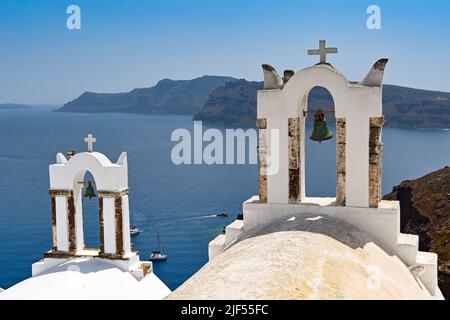 Oia, Santorini, Griechenland - 2022. Juni: Glocken auf der Spitze einer Kirche mit Blick auf das Meer in der Stadt Oia. Stockfoto