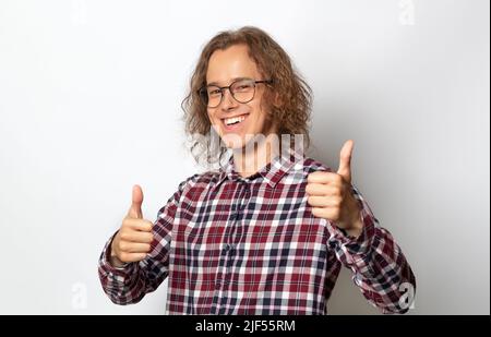 Erfolgreicher junger Mann mit Brille, Student, zeigt eine Geste der Zufriedenheit, Daumen hoch. Stockfoto