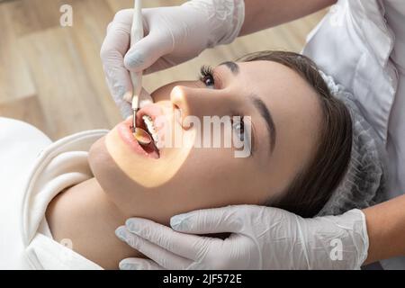 Junge Frau mit zahnärztlichen Check-up in der Zahnklinik. Zahnarzt, der die Zähne eines Patienten mit einem Zahnspiegel untersucht Stockfoto