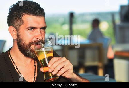 Bärtiger Mann mit einem Glas Bier. Bier. Fröhlicher junger Mann, der ein Glas Bier in der Hand hält und die Kamera anschaut. Stockfoto