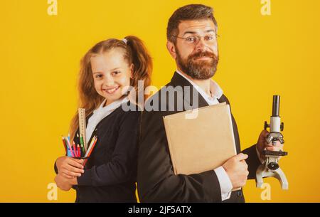 Lehrer mit glücklichen Schüler Schulmädchen. Porträt von lustigen Schulmädchen und Tutor mit Schulbedarf. Glückliche Lehrerin und Schülerin Mädchen auf gelb. Zurück zu Stockfoto