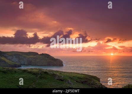 Nach Tagen starker Winde und Regen heben sich die Gewitterwolken am Horizont, wenn die Sonne über dem South West Coast Path im Rocky Valley bei Trethevy untergeht Stockfoto