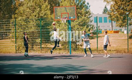 Vier junge Männer spielen Basketball auf dem Sportplatz im Freien Stockfoto