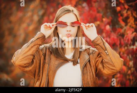 Porträt einer lustigen Frau mit Herbstblättern. Herbstliches weibliches Gesicht. Schöne Mädchen Frau hält in ihren Händen gelben Ahornblätter über ihr Auge. Stockfoto