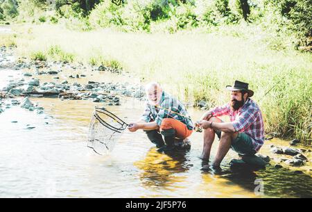 Angelteam. Brutale Männer, die in der Nähe des Flusswassers sitzen. Weiter angeln. Spaß und Entspannung. Angler fangen die Fische. Viel Vergnügen. Entspannen Sie sich in der Natur Stockfoto