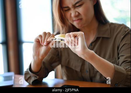 Wütend und wütend Millennial asiatische Frau brechen eine Kreditkarte oder Debitkarte mit ihren Händen, die finanzielle Probleme. Stockfoto