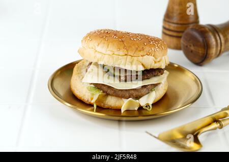 Hausgemachter Premium Cheese Hamburger auf Golden Plate, weißer Tisch Stockfoto