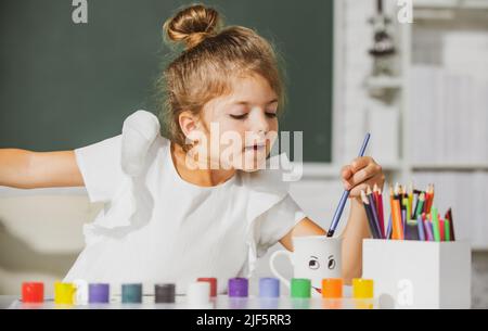 Kind Mädchen zieht im Klassenzimmer sitzen an einem Tisch, Spaß auf der Schule Tafel Hintergrund. Frühkindliche Bildung. Stockfoto