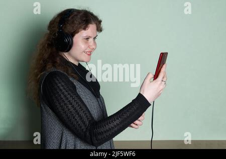 Die Studioaufnahme einer hübschen Frau, die mit Smartphone und Kopfhörern Selfis macht. Lifestyle mit Technologie. Stockfoto