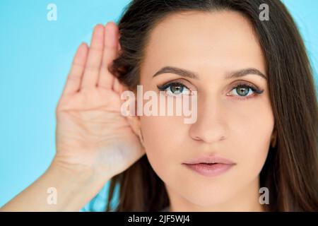 Die Frau hält ihre Hand nahe am Ohr und hört aufmerksam zu Stockfoto