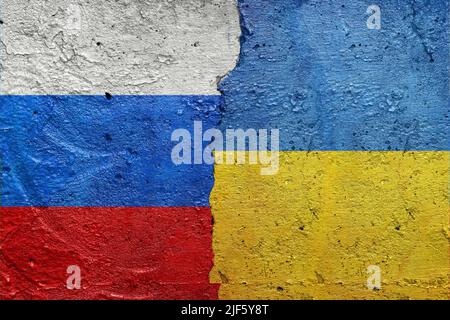 Russland gegen die Ukraine - eine zerrissene Betonwand, die mit einer ukrainischen Flagge auf der linken Seite und einer russischen Flagge auf der rechten Seite bemalt ist Stockfoto