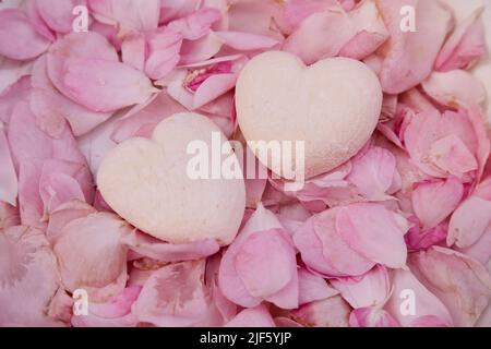 Hausgemachte natürliche zuckerfreie Vanille-Sümpfe Herzen auf Rosenblüten. Gesunde Süßigkeiten, natürliche Nahrung. Romantischer Hintergrund. Stockfoto