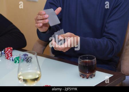 Man's Hands shuffling Karten in einem Poker-Spiel. Chips, Karten, Glas Whiskey auf dem Tisch mit Spiegelung. Poker Club. Stockfoto