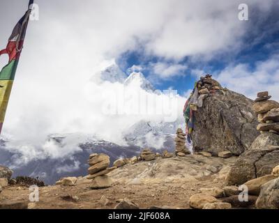 Gebetsfahnen und cairns markieren einen Aussichtspunkt (4600m) auf dem Grat, der zum Nangkartshang Peak führt. AMA Dablam ist durch die Maiwolken kaum sichtbar. Stockfoto