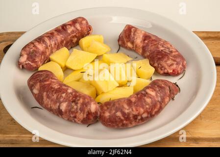 Verbinden Sie Würste mit frisch gebackenen Kartoffeln auf Holzschneidebrett isoliert auf weiß mit Kopierplatz. Stockfoto