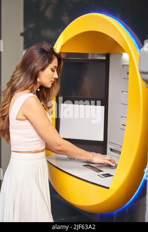 Stilvolle Frau, die einen Geldautomaten im Freien auf der Straße benutzt. Geld-, Banken- und Urban-Lifestyle-Konzept. Stockfoto