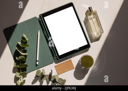 Kreativer Raum mit Tablet und leerem Bildschirm, Blumen, Visitenkarte und Parfüm. Frau Designer Arbeitsbereich Modell, Draufsicht. Natürliches Licht mit Schatten Stockfoto