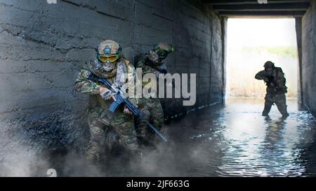 Foto von drei Söldnern während einer Sonderaktion vor dem Hintergrund eines Betontunnels aus unterirdischem Bunker und Rauch. Collage - Stockfoto