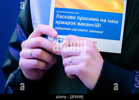 Berlin, Deutschland. 02.. Juni 2022. Auf einer von der Berliner Industrie- und Handelskammer und der Arbeitsagentur organisierten Jobmesse für ukrainische Flüchtlinge hält eine Frau den fairen Plan mit der ukrainischen Flagge. Der Arbeitsmarkt hatte sich bisher trotz Krisen und weit verbreiteter Materialknappheit in der Industrie als stabil erwiesen. Experten hatten jedoch bereits davor gewarnt, dass der Ukraine-Krieg auch den Arbeitsmarkt im Südwesten beeinflussen könnte. (Zur dpa 'Arbeitslosigkeit stieg im Juni aufgrund der Registrierung von Ukrainern') Quelle: Christoph Soeder/dpa/Alamy Live News Stockfoto