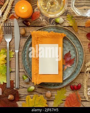 Herbst rustikale Tischeinstellung mit leerer Platzkarte und Umschlag zwischen bunten Blättern und Beeren, Draufsicht, Mockup. Flach legen Horizontale Karte auf Holz Stockfoto