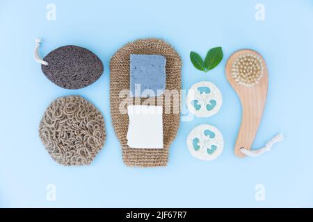 Natürliches Badezubehör für die Körperpflege auf blauem Hintergrund - Holzbürste, Körperpeeling, Loofah-Schwamm, Bimsstein, natürliches Hanf-Badetuch und Bad Stockfoto