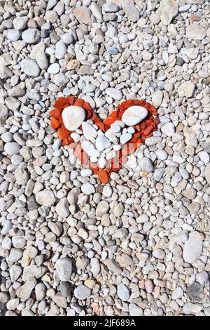 Rote Herzform aus Strandsteinen und Kieselsteinen. Valentinstag-Symbol. Stockfoto