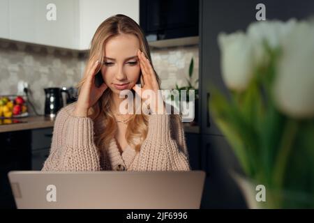 Junge attraktive Frau in Großstrick-Jacke von erlebt wenig Stress, während sie zu Hause an ihrem Laptop arbeitet. Stockfoto