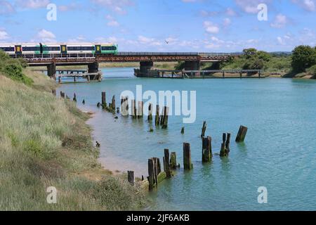 Ein südlicher Personenzug überquert den Fluss Arun bei Ford, in der Nähe von Littlehampton, West Sussex. Zeigt Reste von Holzsteg im Vordergrund. Stockfoto