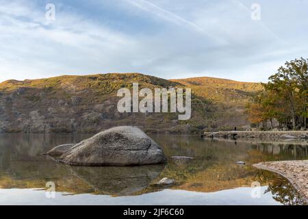 Der Sonnenuntergang spiegelte sich auf einem Gletschersee mit einem großen Felsen wider. Sanabria Lake Stockfoto