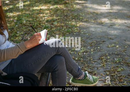 Geballte Frau, die auf einem Notizbuch auf einer Bank in einem Park sitzt Stockfoto