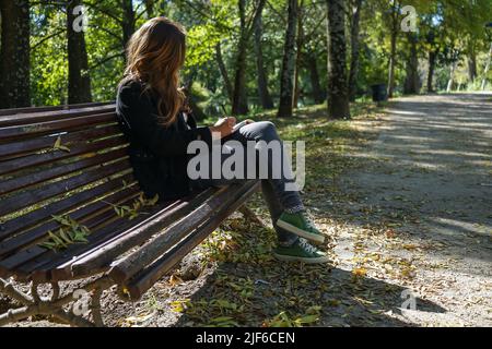 Geballte Frau, die auf einem Notizbuch auf einer Bank in einem Park sitzt Stockfoto