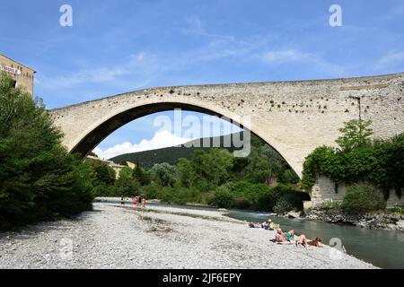 Touristen, die sich am Aigues-Fluss unter der Mittelalterbrücke Single Span, bekannt als Römische Brücke, Nyons Drôme Provence France, sonnen und entspannen Stockfoto