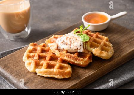 Trendiges Frühstück mit Broffles, Morgenkaffee und Ahornsirup auf Holzschneidebrett auf braunem Hintergrund. Croissant als Waffel. Nahaufnahme. Stockfoto