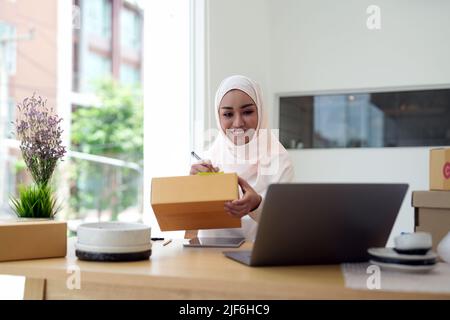 Glückliche junge muslimische Frau Besitzer Schreiben Adresse auf Karton, junge Besitzerin Frau Start Up for Business Online. Menschen mit Online-Shopping KMU Stockfoto