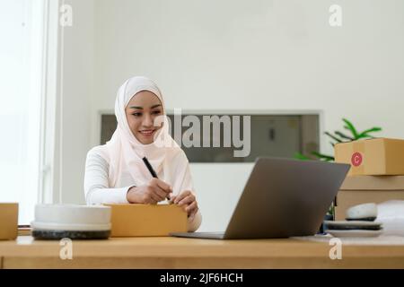 Glückliche junge muslimische Frau Besitzer Schreiben Adresse auf Karton, junge Besitzerin Frau Start Up for Business Online. Menschen mit Online-Shopping KMU Stockfoto